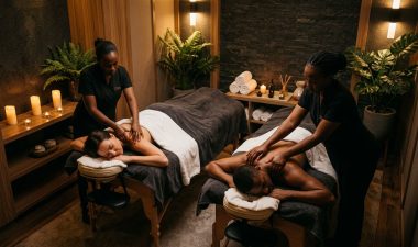Two partners receive massages on adjacent tables in a warmly lit spa room.